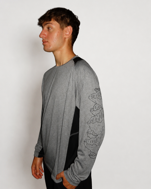 A man wearing a heather gray long-sleeve shirt with black side panels and a black mountain line-art graphic on the sleeve, shown in profile against a plain light gray background.